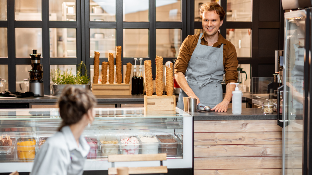 An ice cream shop owner talks to an employee while serving ice cream.