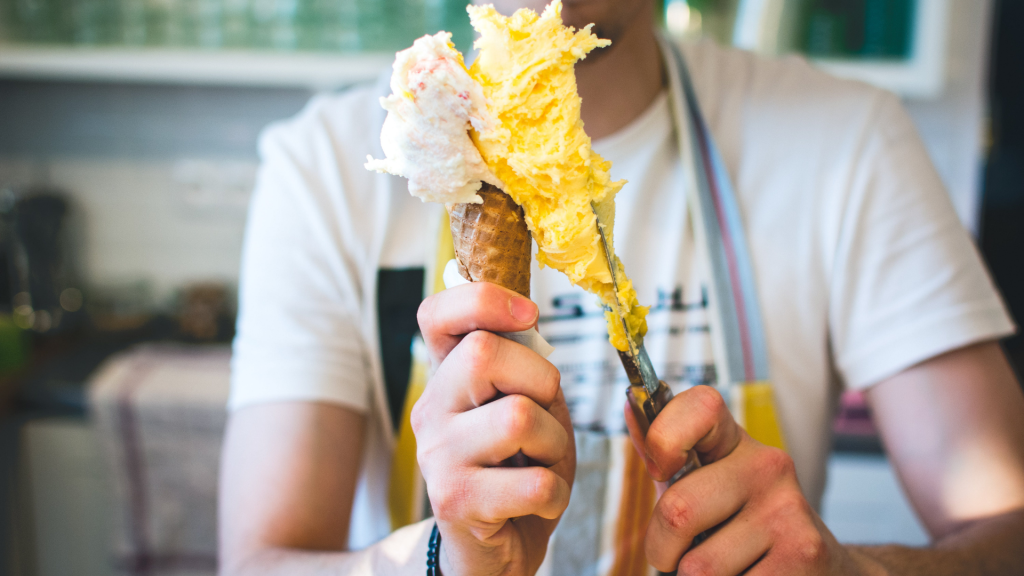 An ice cream shop employee serves ice cream on a cone.