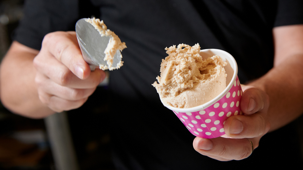 An ice cream shop employee serves a cup of ice cream.